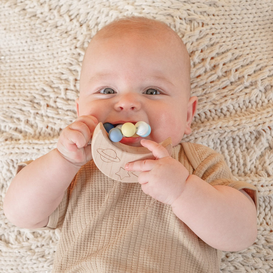 Baby holding a wooden teether with silicone beads during supervised play