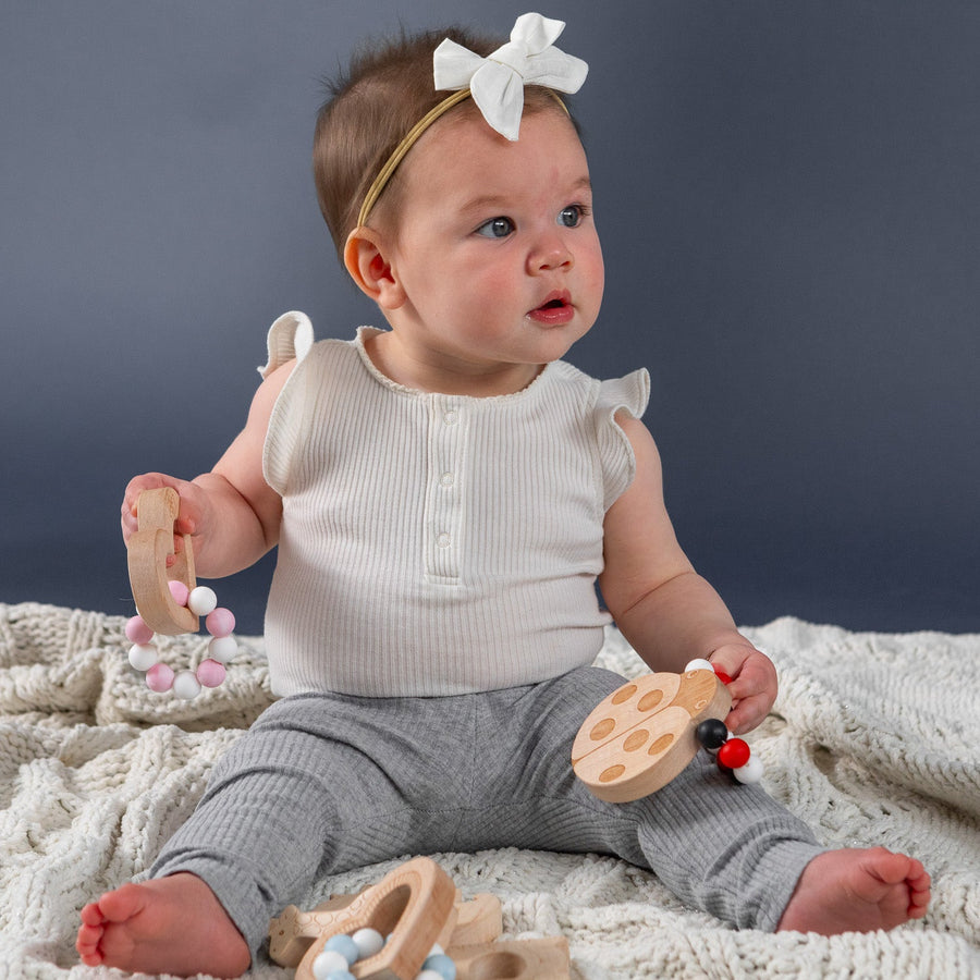 Baby holding a wooden teether with silicone beads during supervised play