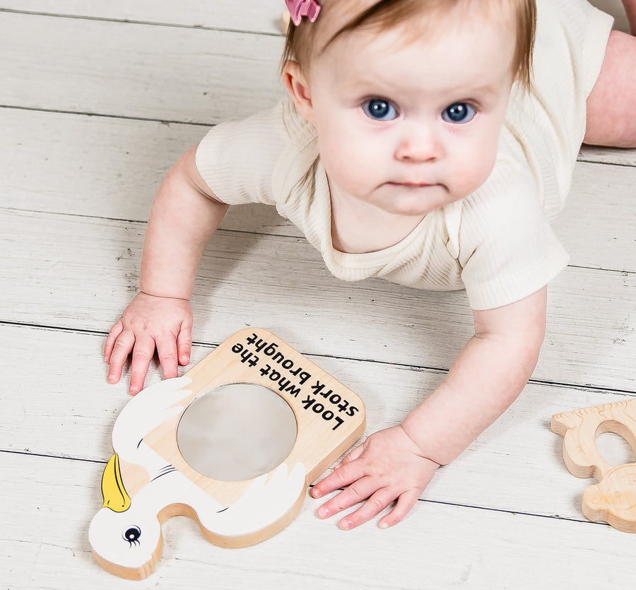 Baby exploring a stork-shaped wooden discovery mirror