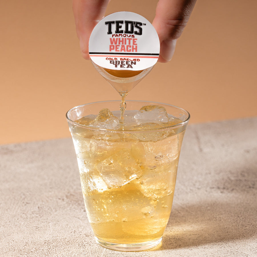 Hand pouring Ted’s White Peach tea into iced water