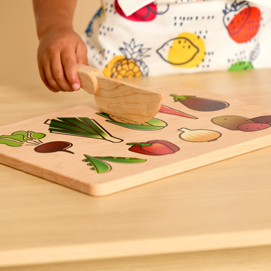 Child using a wooden knife and illustrated cutting board during food preparation