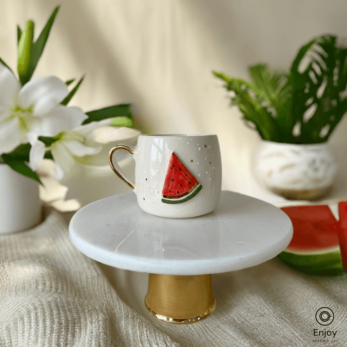 A charming handmade mug featuring a vibrant 3D watermelon slice, resting elegantly on a golden pedestal, with soft natural light illuminating the scene.