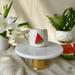 A charming handmade mug featuring a vibrant 3D watermelon slice, resting elegantly on a golden pedestal, with soft natural light illuminating the scene.