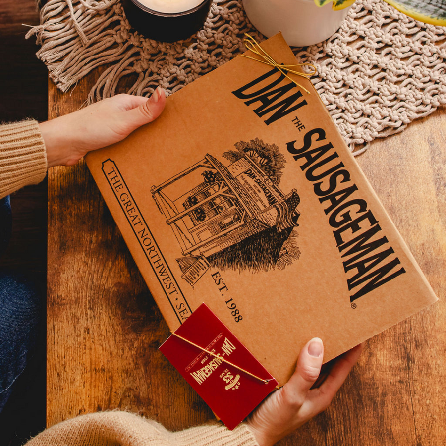 Hands holding a closed Dan The Sausageman kraft gift box with red tag