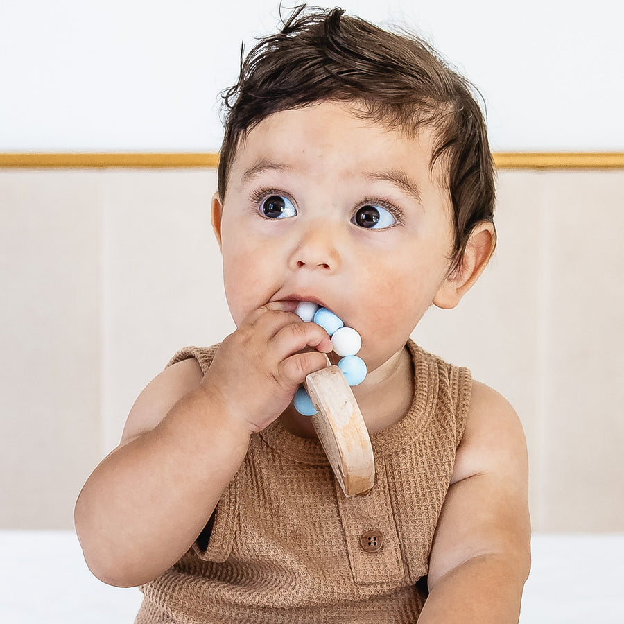 Baby holding a wooden teether with silicone beads during supervised play