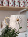 Handmade ceramic mug featuring a delicate daisy flower design with a golden center, displayed on a marble stand with festive pine decor.