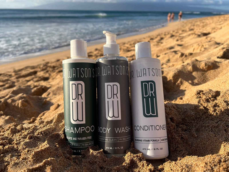 Three Dr. Watson's shower care bottles on a sandy beach