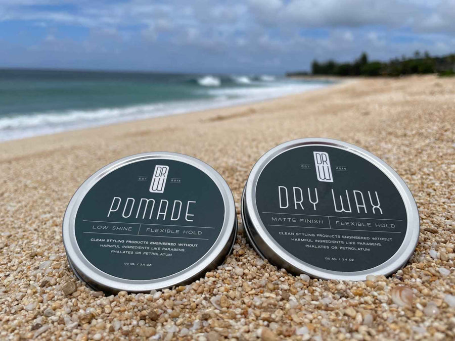 Dr. Watson's pomade and Dry Wax jars on a beach