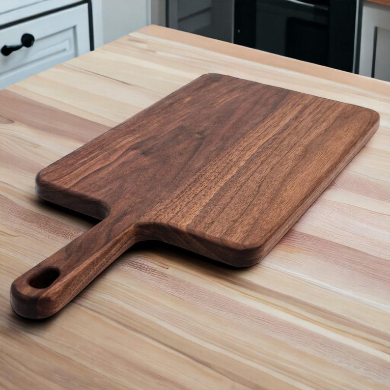 Wide walnut paddle serving board resting on a kitchen counter