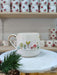 Handmade ceramic mug featuring a whimsical forest scene with trees, mushrooms, and a tiny house in vibrant colors, accented with a golden-rimmed handle. Displayed on a marble stand with festive touches, this mug brings a magical woodland charm to your everyday coffee or tea moments.
