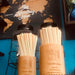 Wooden holders filled with eco-friendly straws from Holy City Straw Co., displayed on a counter with glass jars and a 'Big Travelling Man' sign in the background.
