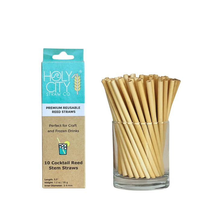 A turquoise-and-brown branded box labeled ‘HolyCity Straw Co. Premium Reusable Reed Straws’ next to a clear glass container filled with multiple short, natural reed straws. The packaging specifies ‘Perfect for Craft and Frozen Drinks’ and ‘10 Cocktail Reed Stem Straws.
