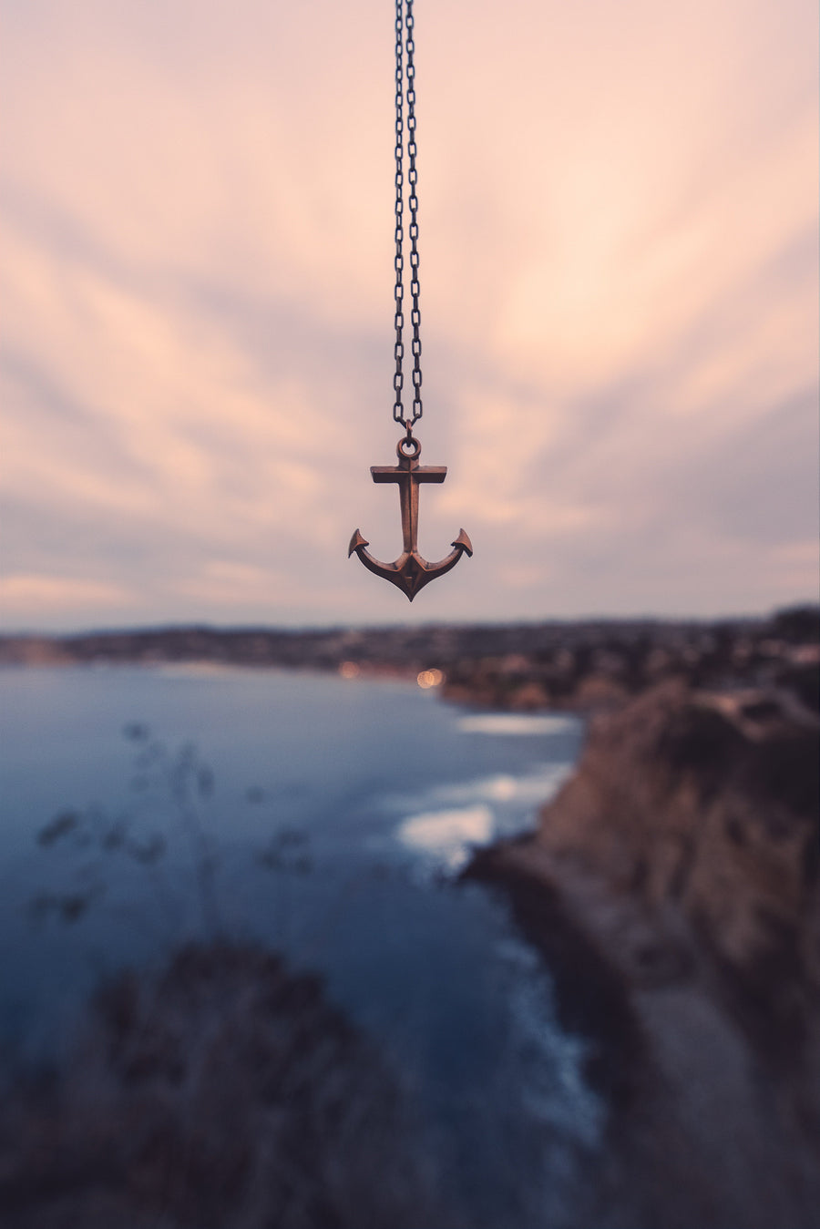Anchor necklace photographed against a coastal landscape