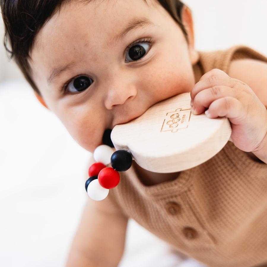 Baby holding a wooden teether with silicone beads during supervised play