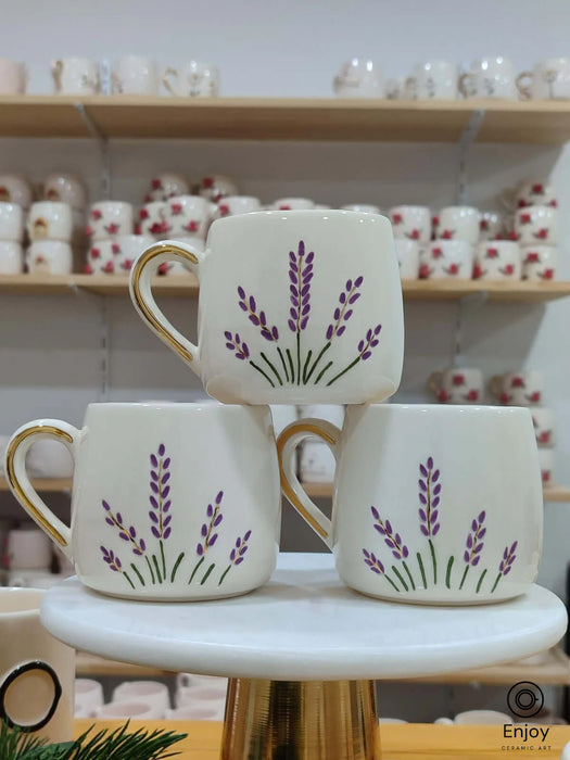 A trio of handcrafted ceramic mugs adorned with delicate lavender sprigs, each topped with a touch of gold on the handle, perfect for bringing a hint of nature’s calm to your coffee ritual.