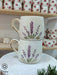 Stacked handmade ceramic mugs adorned with lavender stems in purple and gold accents, featuring gold-rimmed handles. Displayed elegantly in a cozy setting with floral-themed mugs on wooden shelves. Perfect for adding a touch of nature to your coffee moments.