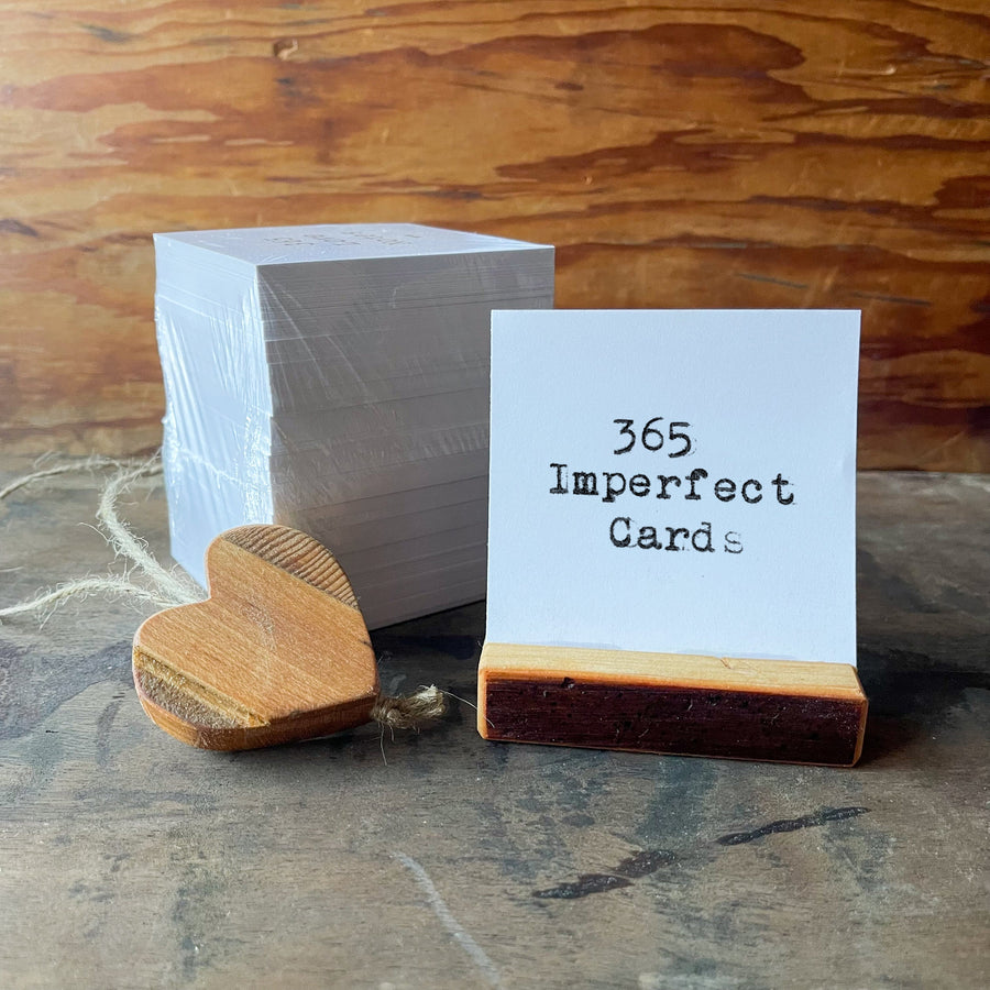 365 Imperfect Cards title card in a wooden stand beside small hearts.