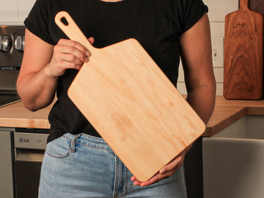 Person holding a wide maple paddle serving board