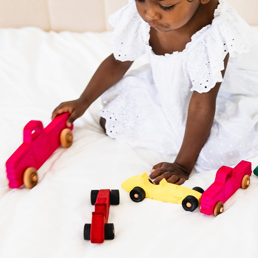 Child arranging colorful wooden toy cars and pickup trucks