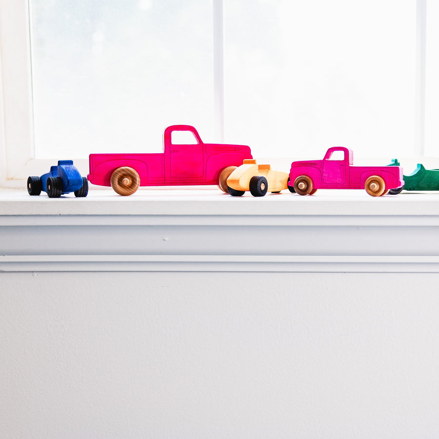 Colorful wooden toy pickup trucks lined up on a windowsill