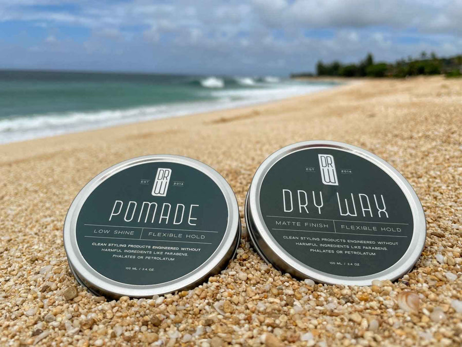 Dr. Watson's pomade and Dry Wax jars on a beach