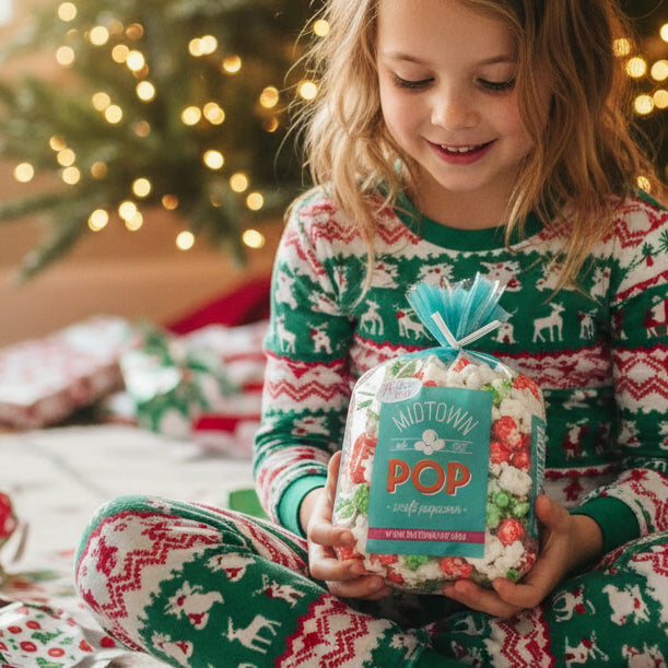 Child holding Christmas popcorn beside a tree