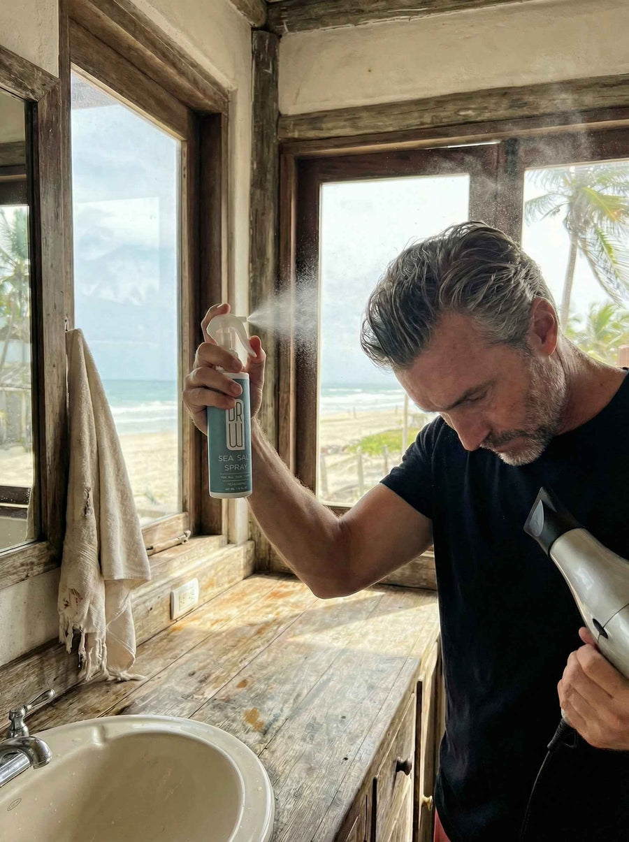 Person spraying sea salt styling product onto hair by a mirror