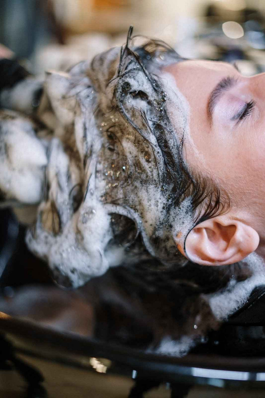 Shampoo lather being worked through wet hair at a salon sink