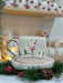 Festive snowman-themed espresso cup with gold accents, paired with a saucer, nestled in holiday greenery for a cozy Christmas vibe.