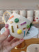 A vibrant handmade ceramic mug featuring colorful 'sprinkle' designs in various shapes and gold accents, with a gold handle, perfect for adding a playful touch to your coffee moments.