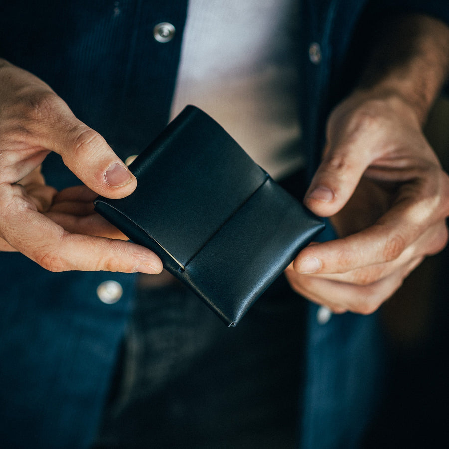 Navy Franklin leather wallet, held in both hands with the front flap visible