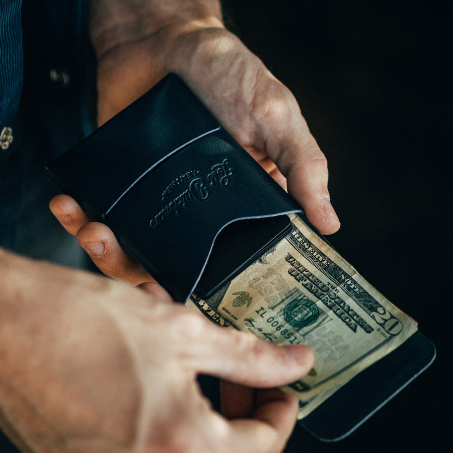Navy Franklin leather wallet, held open while a bill is inserted