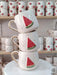 Handmade ceramic mugs featuring a vibrant watermelon slice design, displayed on a marble stand.