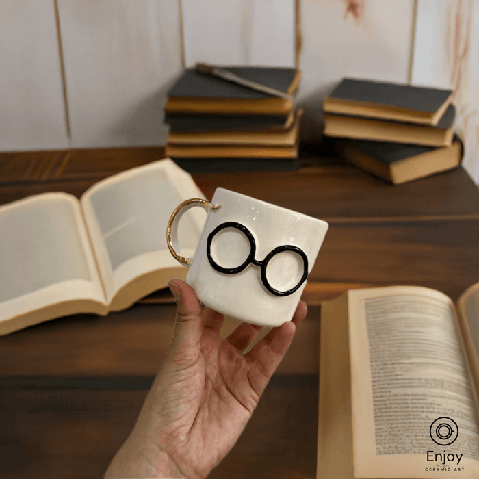 A magical mug with round glasses and a gold handle, held against a backdrop of open books and vintage volumes.
