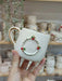 A handmade ceramic mug featuring a 3D Christmas wreath design with red, green, and gold accents, paired with a gold handle, perfect for holiday celebrations.
